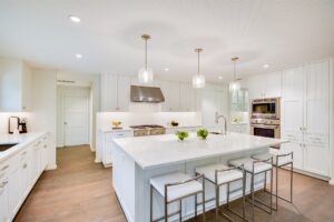 Bright kitchen with white cabinets, a large island with stools, pendant lights, and stainless steel appliances.