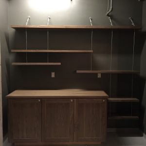 Wooden cabinet with three doors and wall-mounted shelves on a dark painted wall with visible electrical outlets.