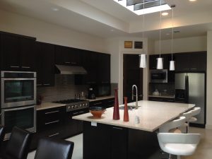 Modern kitchen with dark cabinets, stainless steel appliances, island with white chairs, and pendant lights.