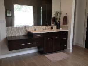 Modern bathroom with a dark wood floating vanity, large mirror, tiled backsplash, and beige tile flooring.
