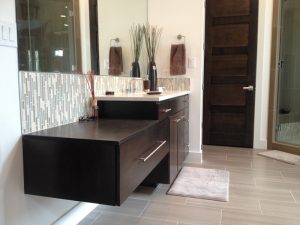 Modern bathroom with a floating dark wood vanity, glass tile backsplash, and decorative items on the counter.