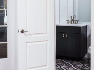 White door opens to a bathroom with a black vanity, white sink, and geometric patterned floor tiles.