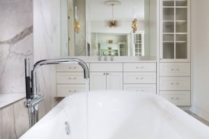 Modern bathroom with a white bathtub, marble walls, vanity with double sinks, and built-in cabinets.
