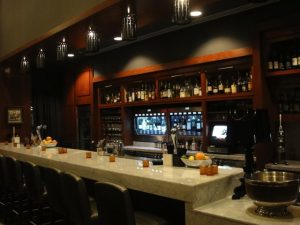 Modern bar with a marble countertop, barstools, shelves of bottles, and pendant lights hanging from the ceiling.