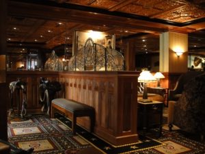 Dimly lit lounge with wood paneling, ornate carpet, leather chairs, and decorative metal dividers.