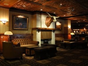 Leather sofas and armchairs surround a fireplace with a bull head mounted above it in a dimly lit, rustic lounge.