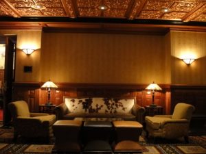 Dimly lit lounge with a cowhide sofa, armchairs, lamps, and a decorative ceiling.