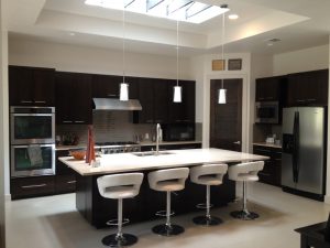 Modern kitchen with dark wood cabinets, stainless appliances, large island, and four white barstools under pendant lights.