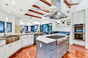 Modern kitchen with white cabinets, stainless steel appliances, center island, and exposed wooden ceiling beams.