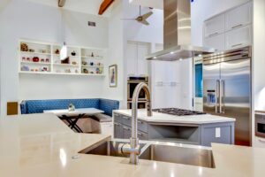 Modern kitchen with stainless steel appliances, island sink, built-in seating nook, and open shelving with decorative items.