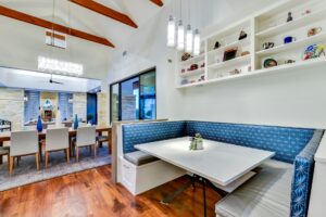 Modern dining area with a built-in blue booth, white table, and open shelves, next to a formal dining room.