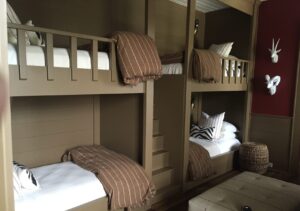 Four built-in bunk beds with brown bedding in a wood-paneled room, featuring animal wall decor and a woven stool.