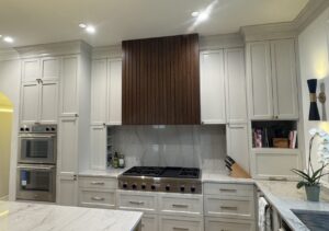 Modern kitchen with white cabinets, marble countertops, stainless stove, and a dark wood range hood.