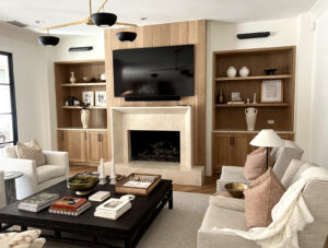 Modern living room with a fireplace, wall-mounted TV, built-in shelves, and neutral-colored furniture and decor.