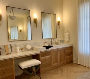 Modern bathroom vanity with double mirrors, marble countertop, wood cabinets, and wall sconces, stool in front.