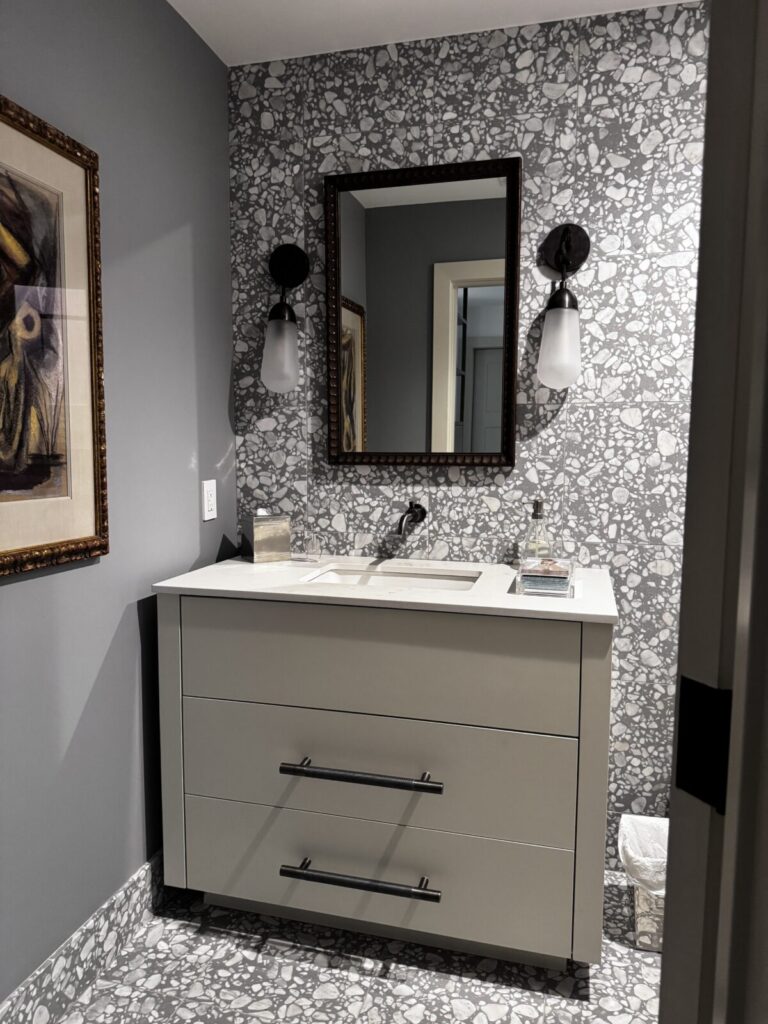 Modern bathroom with patterned tile wall, white vanity, rectangular mirror, and two wall sconces.