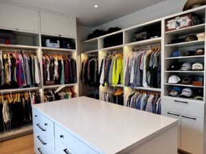 Spacious walk-in closet with hanging clothes, shelves with hats, drawers, and a large white island in the center.