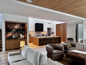Modern open-concept living space with kitchen, bar area, neutral furniture, and wood accents.