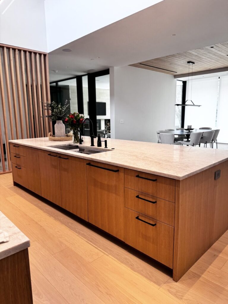Modern kitchen with a large wooden island, black fixtures, and a dining area visible in the background.