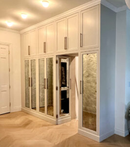 Built-in white wardrobe with mirrored doors, tall cabinets above, and a small open section revealing hanging clothes.