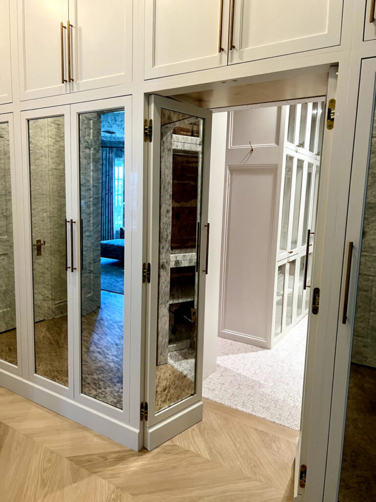 Hidden door in a mirrored closet opens to reveal a bright hallway with built-in shelves and a carpeted floor.
