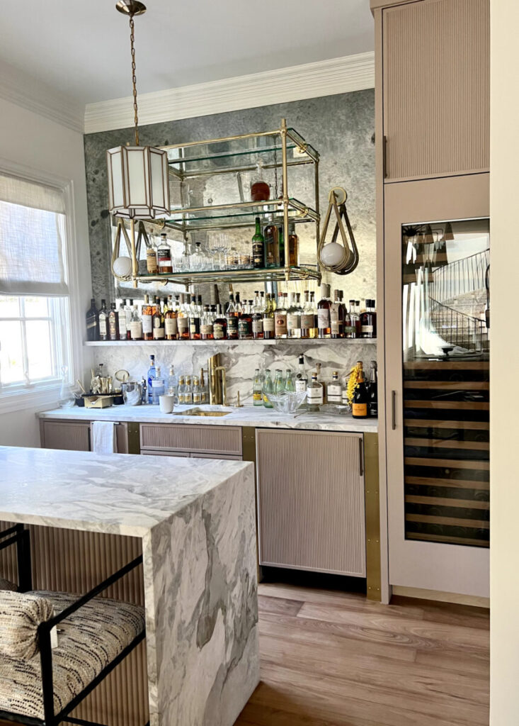 Home bar with marble counter, stocked shelves of liquor bottles, glassware, and a built-in wine fridge.