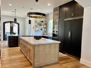 Modern kitchen with wood floors, a large island, dark cabinets, open shelves, and pendant lighting.