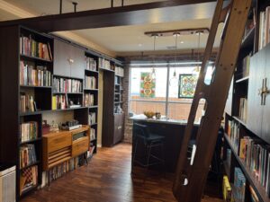 Home library with dark wood shelves, a rolling ladder, a reading nook, and stained glass window panels over a desk.