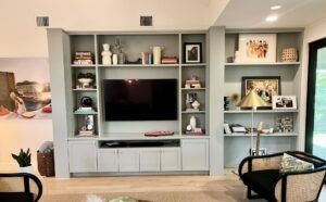 Built-in shelving unit with a TV, books, framed photos, decorative items, and a guitar in a modern living room.