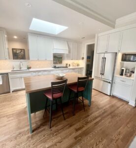 Modern kitchen with white cabinets, a wooden island with two chairs, stainless appliances, and a bowl on the counter.