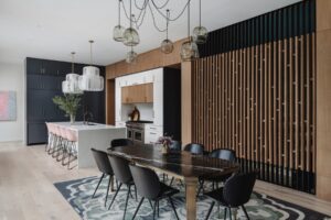 Modern kitchen and dining area with black chairs, marble table, island with pink stools, and pendant lighting.
