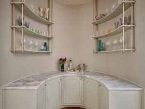 Curved bar area with marble countertop, glass shelves holding glassware, vases, and a bouquet of purple tulips.