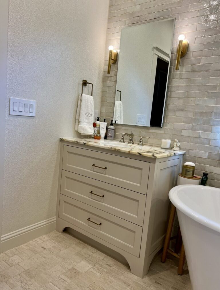 A bathroom vanity with a marble countertop, toiletries, a mirror, towel, and wall lights beside a bathtub.