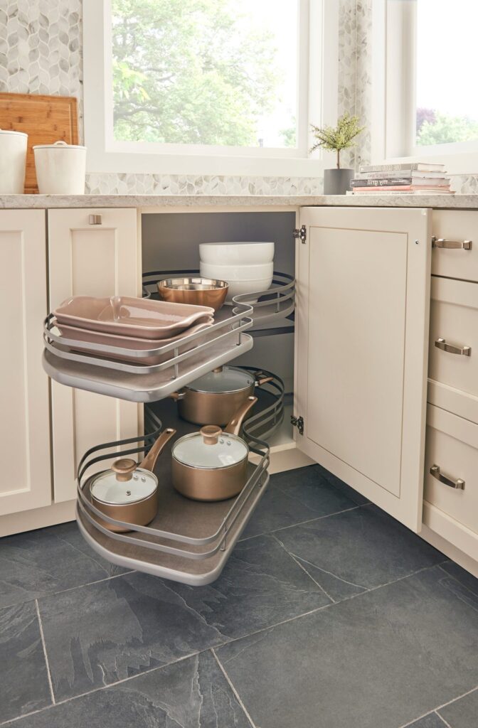 Corner cabinet with pull-out shelves storing pots, pans, and bowls in a modern kitchen with stone tile flooring.