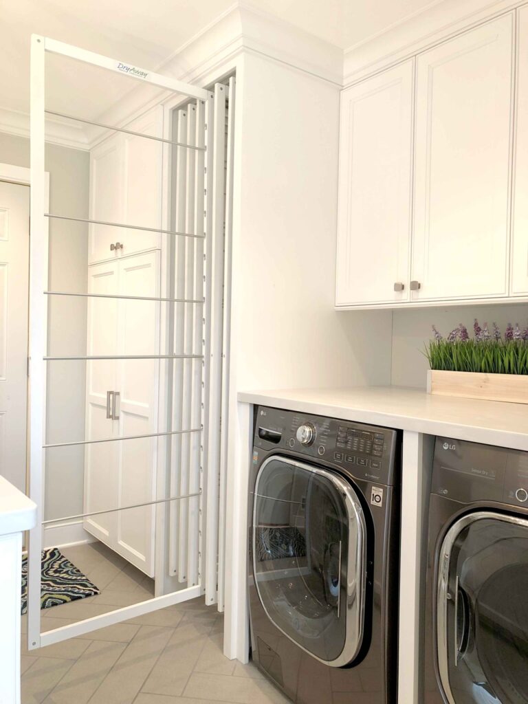 Modern laundry room with a pull-out drying rack, white cabinets, countertop, and front-load washer and dryer.