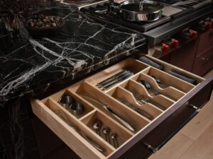 Open kitchen drawer beneath a stove, organized with cutlery, utensils, and napkins in a wooden divider.