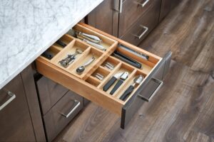 A kitchen drawer with a wooden organizer holds various utensils, cutlery, scissors, and kitchen tools.