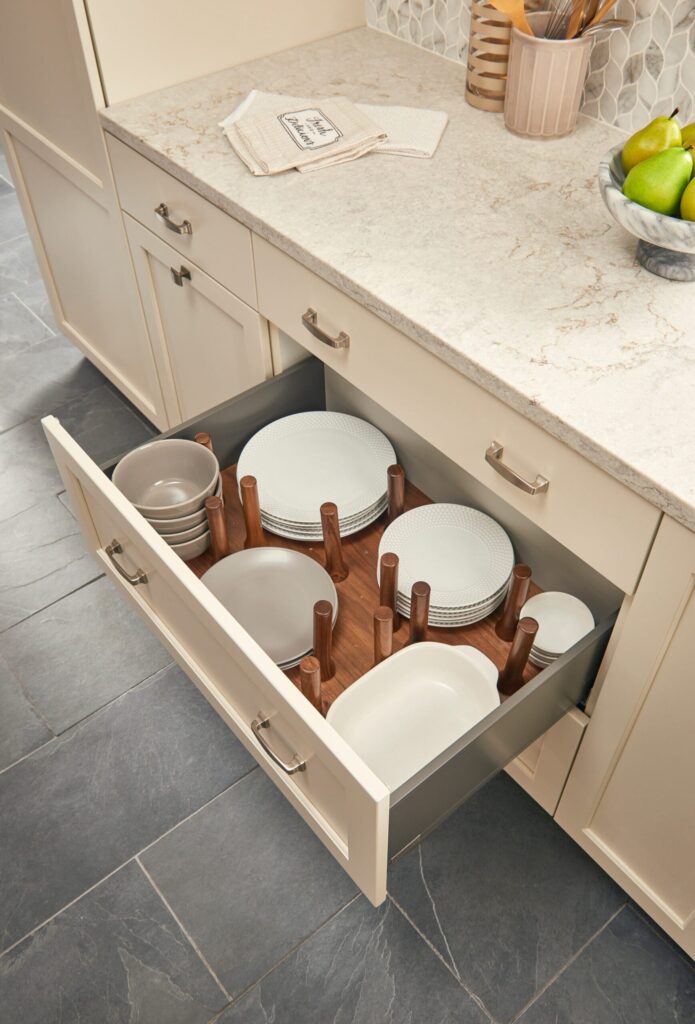 Open kitchen drawer with wooden dividers organizing white plates, bowls, and platters in a neat arrangement.