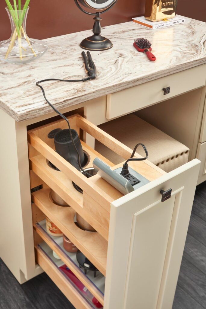 Pull-out cabinet drawer with hairdryer, hair straightener, and power strip beneath a marble countertop.