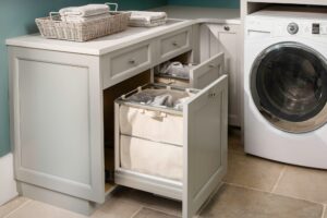 Gray laundry room with a front-load washer, cabinets, pull-out hampers, and folded towels on the countertop.