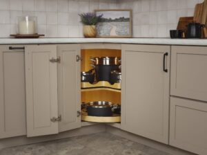 Open corner kitchen cabinet with a lazy Susan shelf holding pots and pans, under beige countertops and decor items.